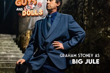 Gangster in blue suit on stairs with hat on knee, Guys and Dolls logo, and text reading Graham Stoney as Bug Jule